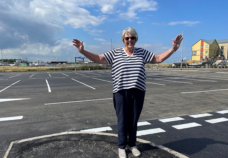 Ann Burke holds arms in the air in front of the new car park