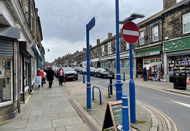 a general scene of Queen Street, Amble with shops, cars and pedestrians